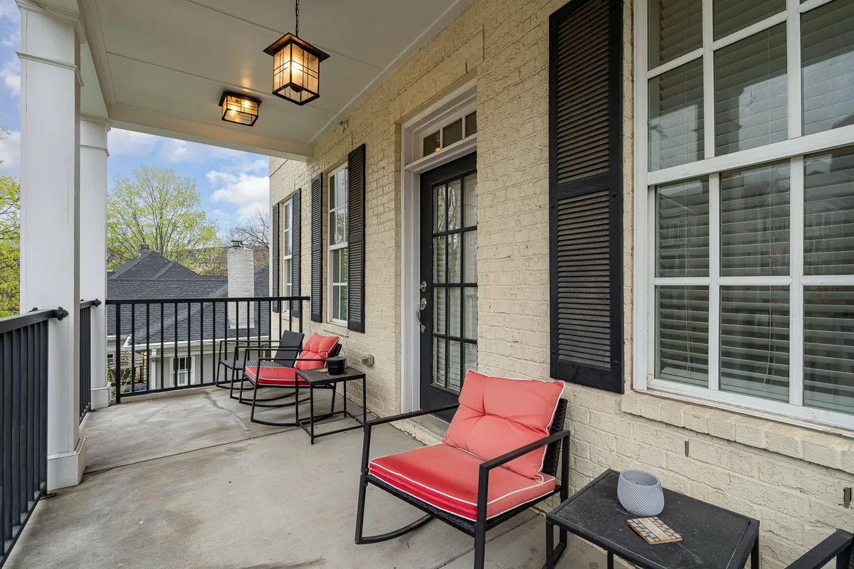 A furnished balcony or porch area featuring red chairs, a black railing, and lanterns adorning the space. The doorway leads back into the home, and the scene conveys an inviting, tranquil atmosphere ideal for morning coffee, reading, or enjoying evening lights.