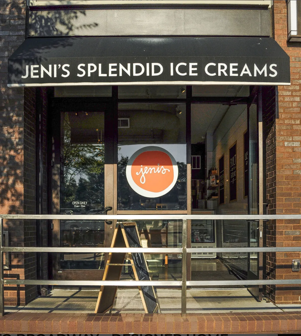 This exterior shot captures the cheerful storefront of Jeni’s Splendid Ice Creams. The bright signage, welcoming glass doors, and visible menu board set the scene for a fun, family-friendly treat outing. Green trees in the background add a lively, neighborhood vibe.