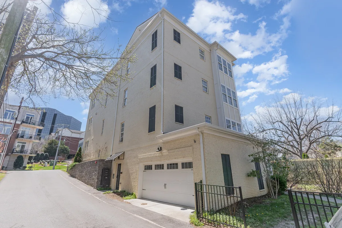 This exterior image features a tall building structure with a large garage door and well-maintained landscaping at the entrance. The visible garage door directly connects to the section's mention of two private garages and secure parking, setting the tone for effortless arrivals.