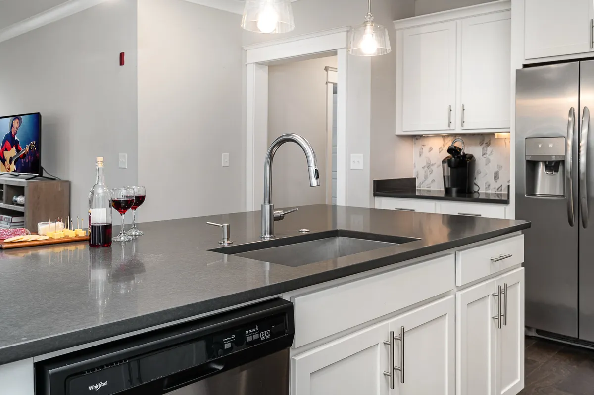 A welcoming kitchen interior with a central island, sink, wine glasses, and a television in the background. The space is set up for cooking, entertaining, and gathering, aligning with amenities like starter kitchen sets and group celebrations.