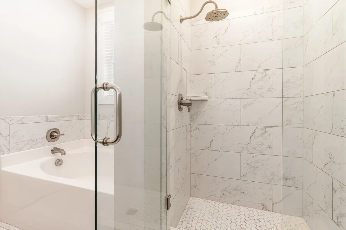 A luxurious bathroom featuring a glass shower enclosure, elegant marble tiles, and a freestanding soaking bathtub. The space exudes a spa-like ambiance, perfect for unwinding after a long day.