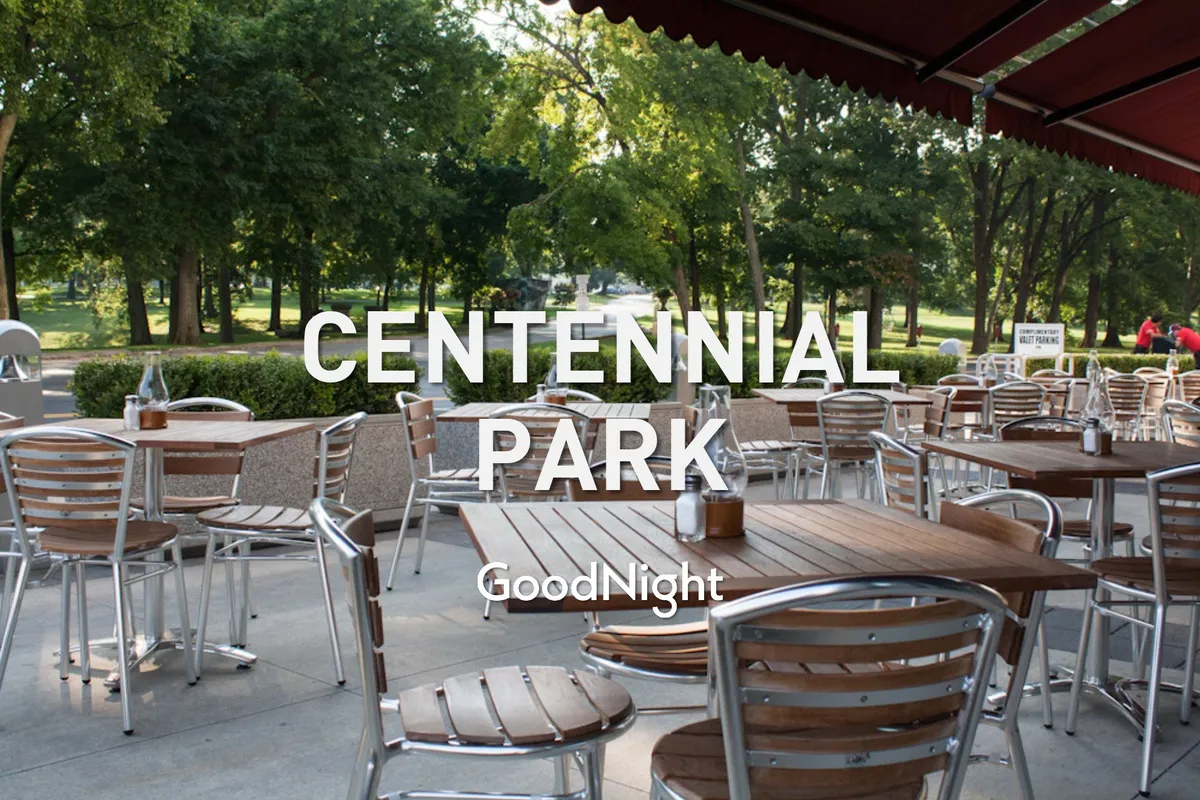 This image presents outdoor dining tables with wooden tops and metal chairs set among green trees, suggesting vibrant opportunities for socializing, networking, or relaxing after a day of work.