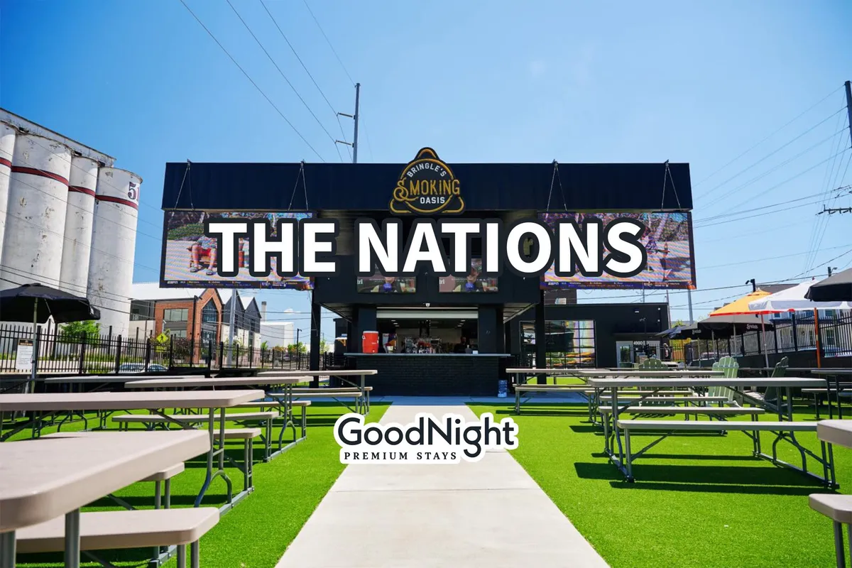 A festive outdoor area featuring large signage reading 'THE NATIONS,' with plenty of outdoor seating arrangements and a food service area. The scene exudes a sense of community, events, and social dining, hinting at local festivities and group-friendly venues.