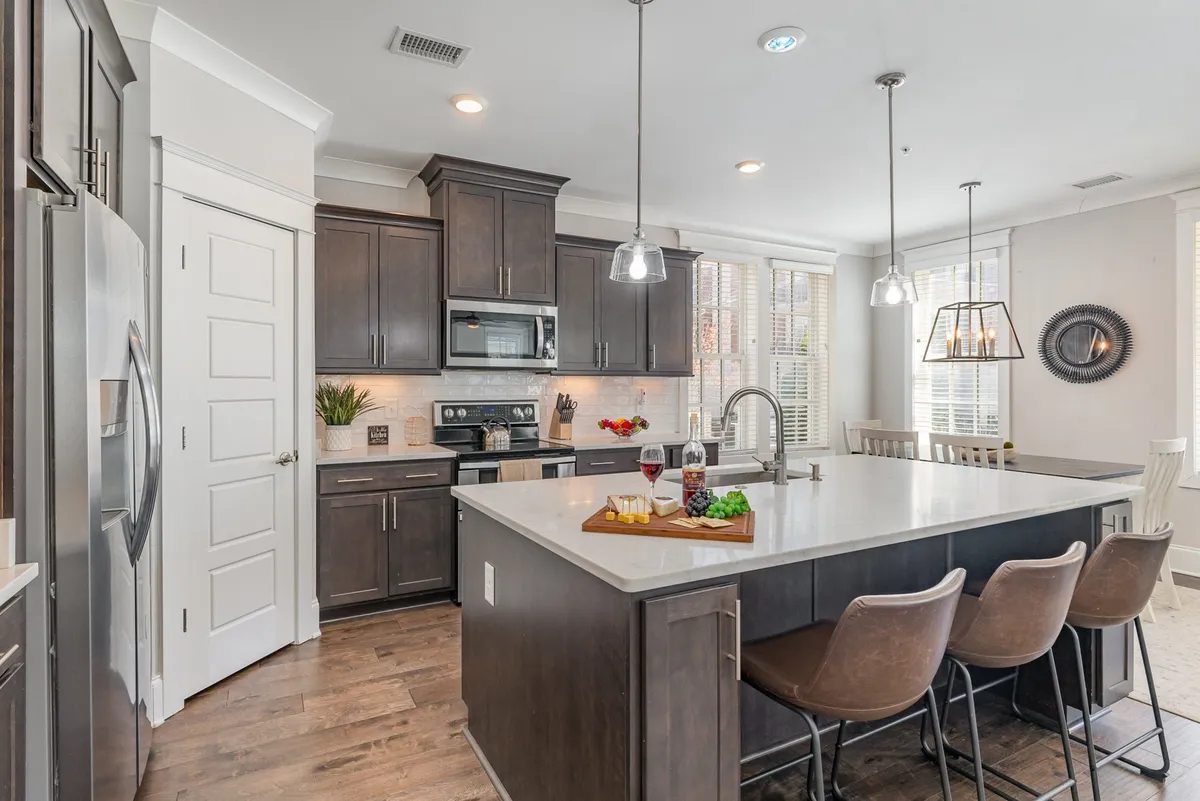 A stylish kitchen with a large island, modern appliances, bar stools, and a dining area in the background. The setting feels both welcoming and contemporary, ideal for cooking, dining, and socializing.