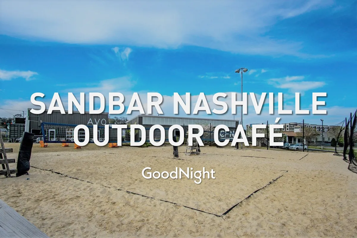 A vibrant outdoor café area with a sand volleyball court in the foreground, surrounded by people socializing, playing volleyball, and enjoying food and drinks as the sun sets. The setting is casual, fun, and evokes the energy of OneCity’s social hub.